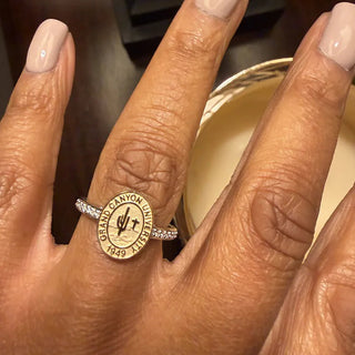 A Grand Canyon University Class Ring | close-up of a hand wearing a GCU graduation ring with a round engraved medallion that reads 'GRAND CANYON University 1949' and a small diamond-studded band.
