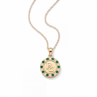 A gold pendant necklace featuring a circular medallion with a gold 'BJ' monogram, surrounded by a halo of small white stones and a border of green stones, suspended from a delicate gold chain on a white background.