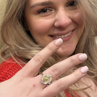 University Of Texas Class Ring | A close-up lifestyle shot of a smiling blonde woman showing off a gold ring with a rose-shaped center stone and small clear accent stones on her finger.